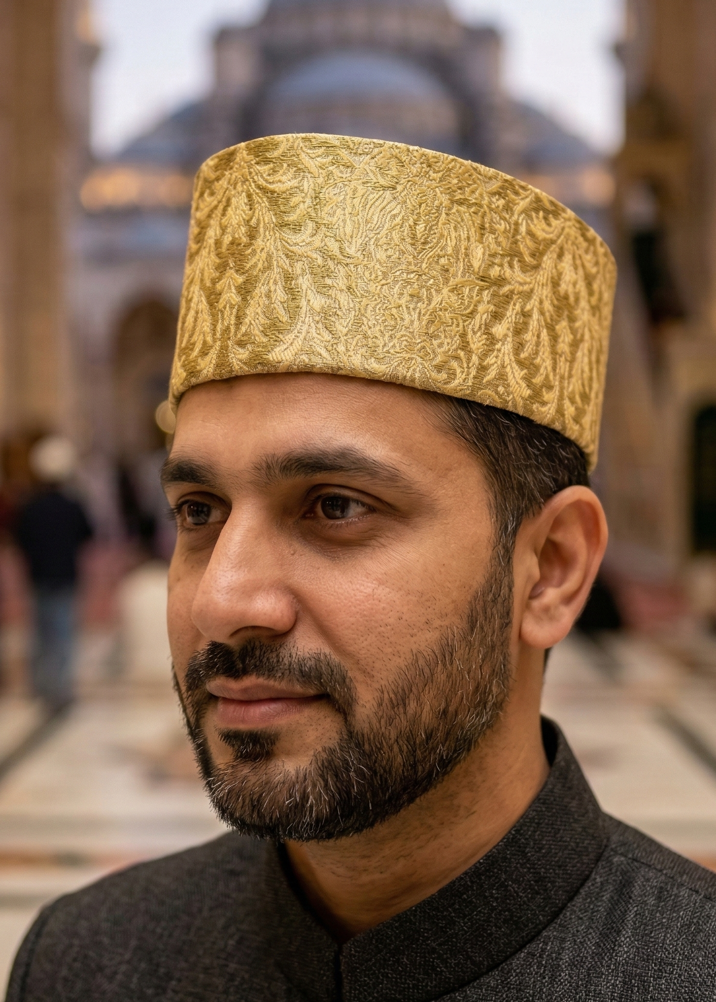 Man wearing a gold embroidered hat in a mosque setting