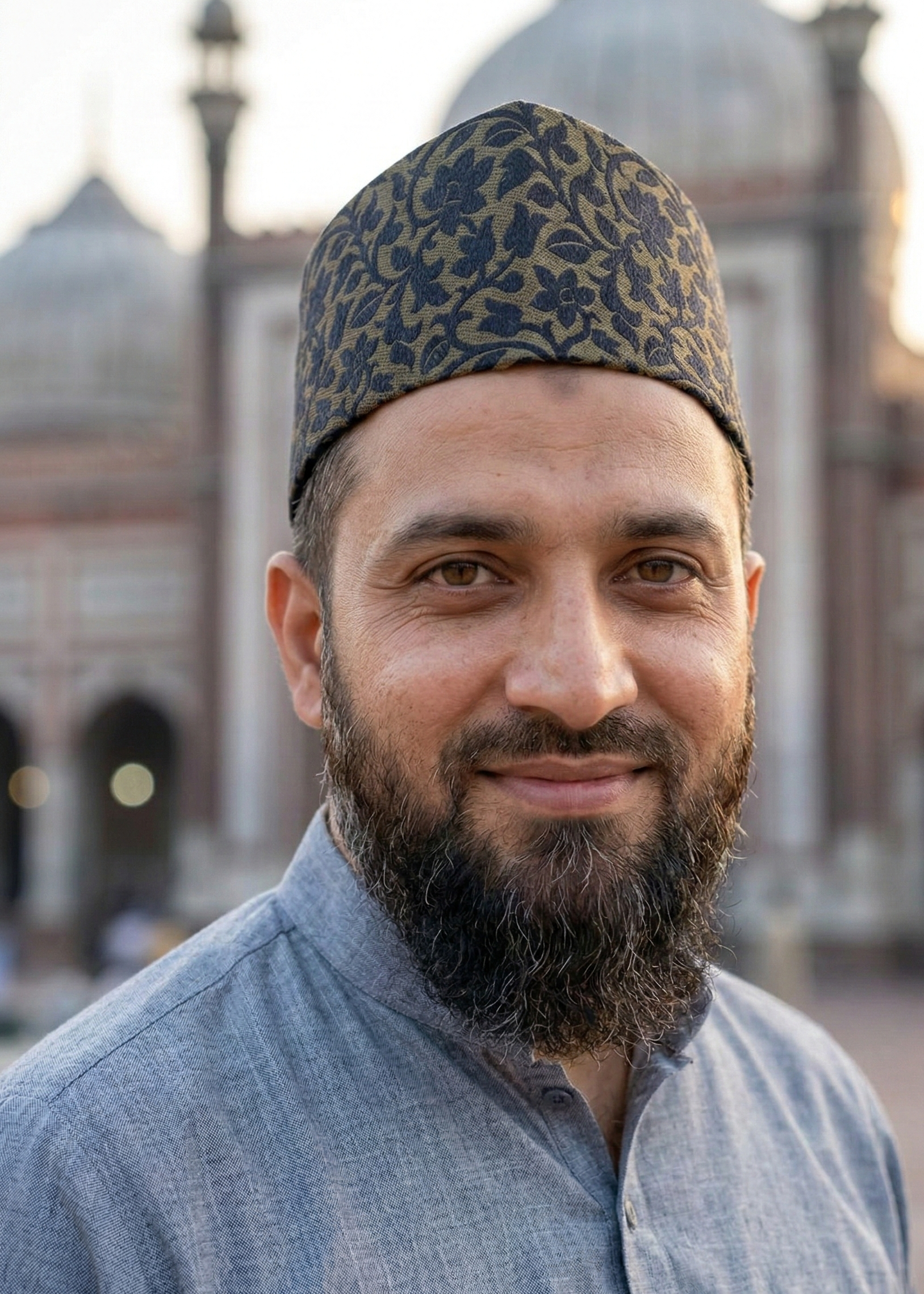 Man wearing a patterned cap and gray shirt in front of a blurred architectural background
