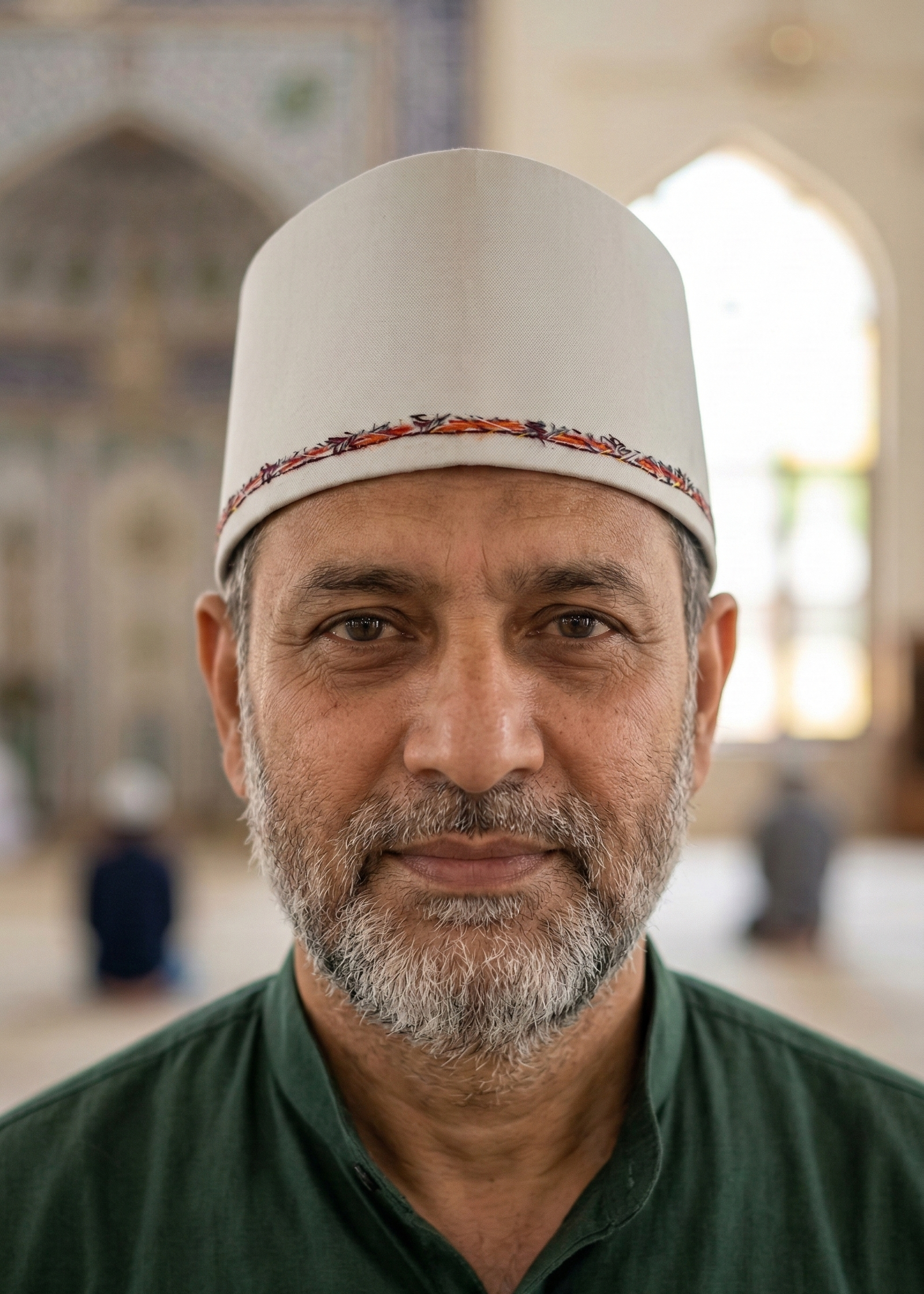 Man wearing a white cap with a decorative band indoors, possibly in a mosque.